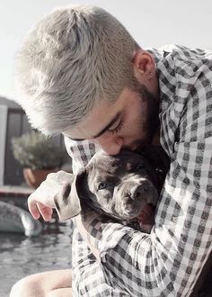 a man holding a dog in his arms while sitting next to a body of water