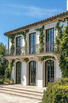 a large white house with lots of windows and plants on the front porch, along with steps leading up to it