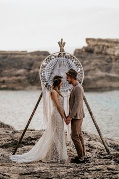 a bride and groom holding hands in front of a water wheel on top of a rocky beach