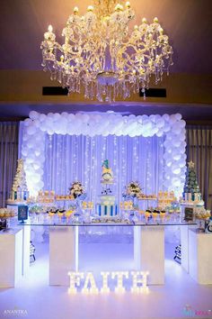 a decorated dessert table with white balloons and blue lights on the ceiling is lit by a chandelier that reads faith