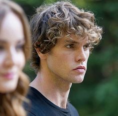 a young man and woman are staring at something in front of them with trees in the background