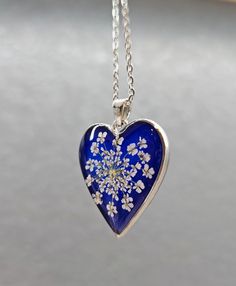 Enjoy this beautiful flower necklace pressed before encapsulating them with resin in an open back bezel. The pendant is 30 x 28 mm Silver Heart and a beautiful chain. The petals have been carefully preserved to retain their color and would make a great gift for your loved ones. This piece was made with real flowers and hence it is important to preserve the jewelry in the box provided safely away from direct sunlight.   You can see more of my Handmade Items here:  https://www.etsy.com/shop/Thecra Resin Necklace With Flower Pendant For Birth Flower, Resin Necklace With Pressed Flower Pendant, White Heart-shaped Jewelry With Pressed Flowers, White Heart Jewelry With Pressed Flowers, Silver Flower Shaped Resin Jewelry, Silver Resin Flower Jewelry, Silver Flower-shaped Necklace With Pressed Flowers, Silver Heart-shaped Jewelry With Pressed Flowers, Silver Heart Jewelry With Pressed Flowers