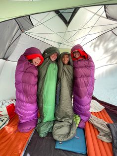 three people in sleeping bags sitting on the inside of a tent