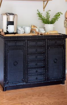 a black cabinet with drawers and cups on top in front of a coffee pot filled with green plants