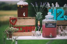 a table topped with bottles and glasses filled with liquid next to wooden crates on top of grass