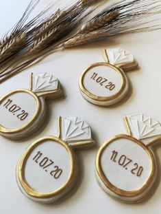 four cookies decorated with gold and white frosting on top of a table next to some wheat