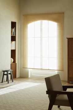 an empty living room with a chair and bookcase in front of a large window