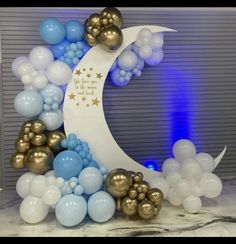 balloon arch with moon and stars on it in front of a wall decorated with blue, gold and white balloons