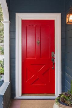 a red front door on a blue house with potted plants in the foreground