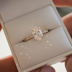 a diamond ring is being held by someone's hand in a white gift box