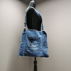 "Upcycled denim shoulder bag with frayed seams, exterior pockets and denim waistband shoulder strap. 15\" wide, 14\" high and shoulder strap measures 32\"." Denim Shoulder Bag With Adjustable Strap, Recycled Denim Shoulder Bag With Pockets Dark Wash, Recycled Denim Shoulder Bag With Pockets In Dark Wash, Dark Wash Recycled Denim Shoulder Bag With Pockets, Upcycled Medium Wash Recycled Denim Shoulder Bag, Vintage Denim Blue Shoulder Bag, Upcycled Medium Wash Cotton Shoulder Bag, Upcycled Denim Hobo Shoulder Bag, Upcycled Denim Shoulder Bag For Everyday Use