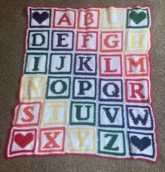 a crocheted blanket that has letters and numbers on it, sitting on the floor