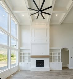 an empty living room with large windows and a ceiling fan in the middle of it