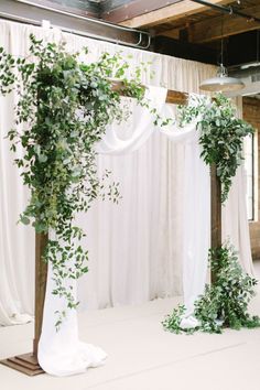 an indoor wedding ceremony with greenery and white draping on the back wall