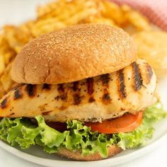 a grilled chicken sandwich with lettuce and tomato on a plate next to french fries