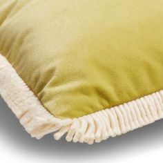 a green pillow with white fringes on the bottom and side, in front of a white background