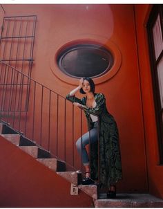 a woman standing on the stairs in front of a red wall with a round window