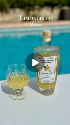 a bottle of lemoncello next to a wine glass on a table near a swimming pool