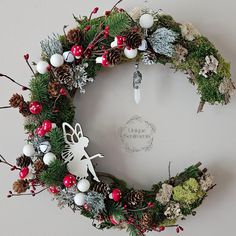 a christmas wreath decorated with pine cones, berries and other holiday decorations is hanging on the wall