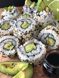 sushi rolls with avocado and sesame seeds on a cutting board next to a jar of sauce