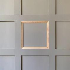 an empty wooden frame hanging on the side of a gray wall with white paneling