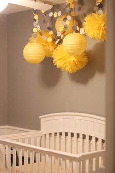 a white crib with yellow pom poms hanging from the ceiling