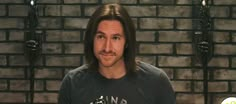 a man with long hair standing in front of a brick wall and looking at the camera