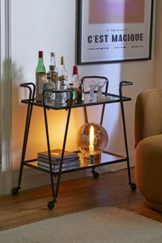 a bar cart with drinks on it in front of a framed poster and orange chair