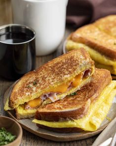 two grilled cheese sandwiches on a plate next to a cup of coffee and spoons