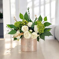 a vase filled with white and green flowers on top of a wooden table next to a couch