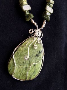 An elegant and eye-catching stone, soft green and flecked with dark green and black, and wrapped in silver in a unique design.  The pendant hangs from a necklace of polished green granite chips and silver beads. The necklace  hangs 19 inches from clasp to top of pendant; the pendant is 1 3/4" high. An easy- to-maneuver silver hook-and-loop clasp completes the necklace. The color and shape of the green jasper caught my eye at a gem show and the stone seemed perfect to become the centerpiece of an unusual necklace. Green Granite, Unusual Necklace, Gem Show, Green Jasper, Jasper Pendant, Green And Black, Silver Beads, Dark Green, Unique Design