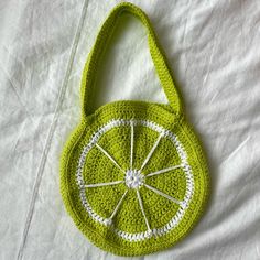 a green crocheted purse with white trim on it sitting on a bed next to a pillow