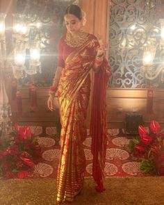 a woman in a red and gold sari standing next to a chandelier