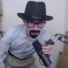 a man with a mustache and glasses holding a microphone in front of his face while wearing a black hat