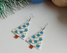 a pair of beaded christmas tree earrings sitting on top of a table next to ornaments