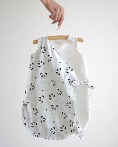 a person holding onto a baby bib with panda faces on it, hanging from a wooden hanger