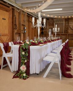 the table is set up with white chairs and red sashers, along with wine glasses