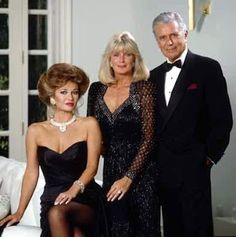 two women and a man in formal wear posing for a photo with one woman sitting on a couch