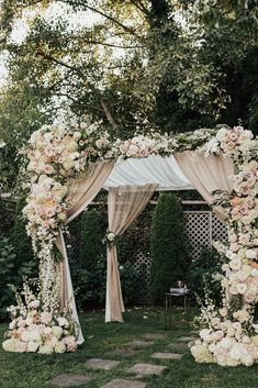 an outdoor wedding ceremony with white and pink flowers on the arch, greenery and stone path