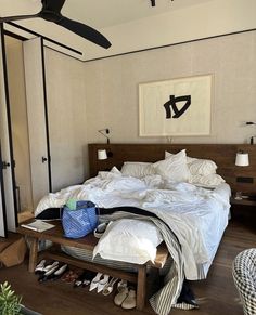 an unmade bed in a bedroom next to a table with shoes on top of it