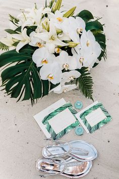 a bouquet of white orchids and two pairs of flip flops on the sand