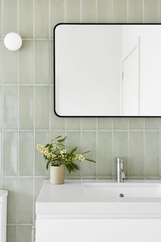 a white sink sitting under a large mirror next to a vase with flowers in it