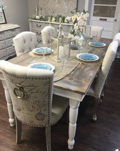 a dining room table with white chairs and blue plates on it's centerpiece