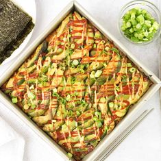 a square casserole dish with vegetables and sauces on the side next to some chopsticks