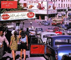 people walking on the sidewalk near cars and billboards