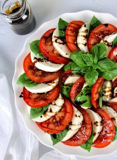 a white plate topped with sliced tomatoes and mozzarella on top of lettuce