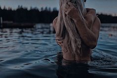 a woman is sitting in the water with her hair blowing back and looking off into the distance