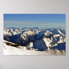 an aerial view of snow covered mountains in the distance with a blue sky above them