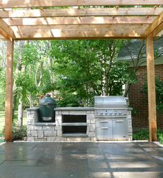 an outdoor bbq with grill and oven under a pergolated area in the back yard