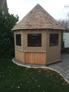 a wooden gazebo sitting on top of a lush green field next to a building